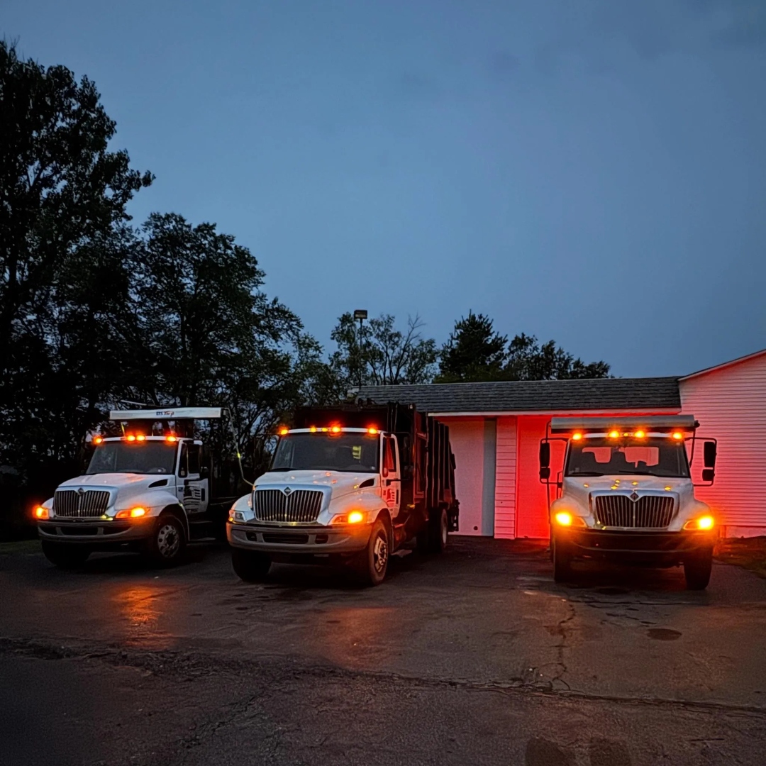 Liberty Sanitation trucks lined up with lights on at dusk