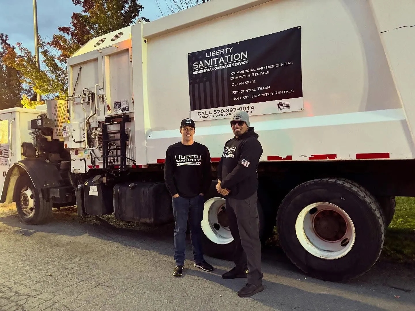 Two Liberty Sanitation team members standing beside a branded garbage truck